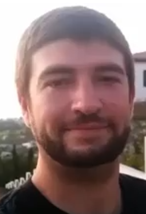 A man with a thick, trimmed beard looking at camera